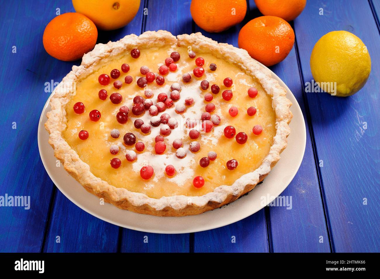 Tasty lemon pie decorated with fresh cranberries and whole orange, lemon and clementines on deep blue table horizontal Stock Photo