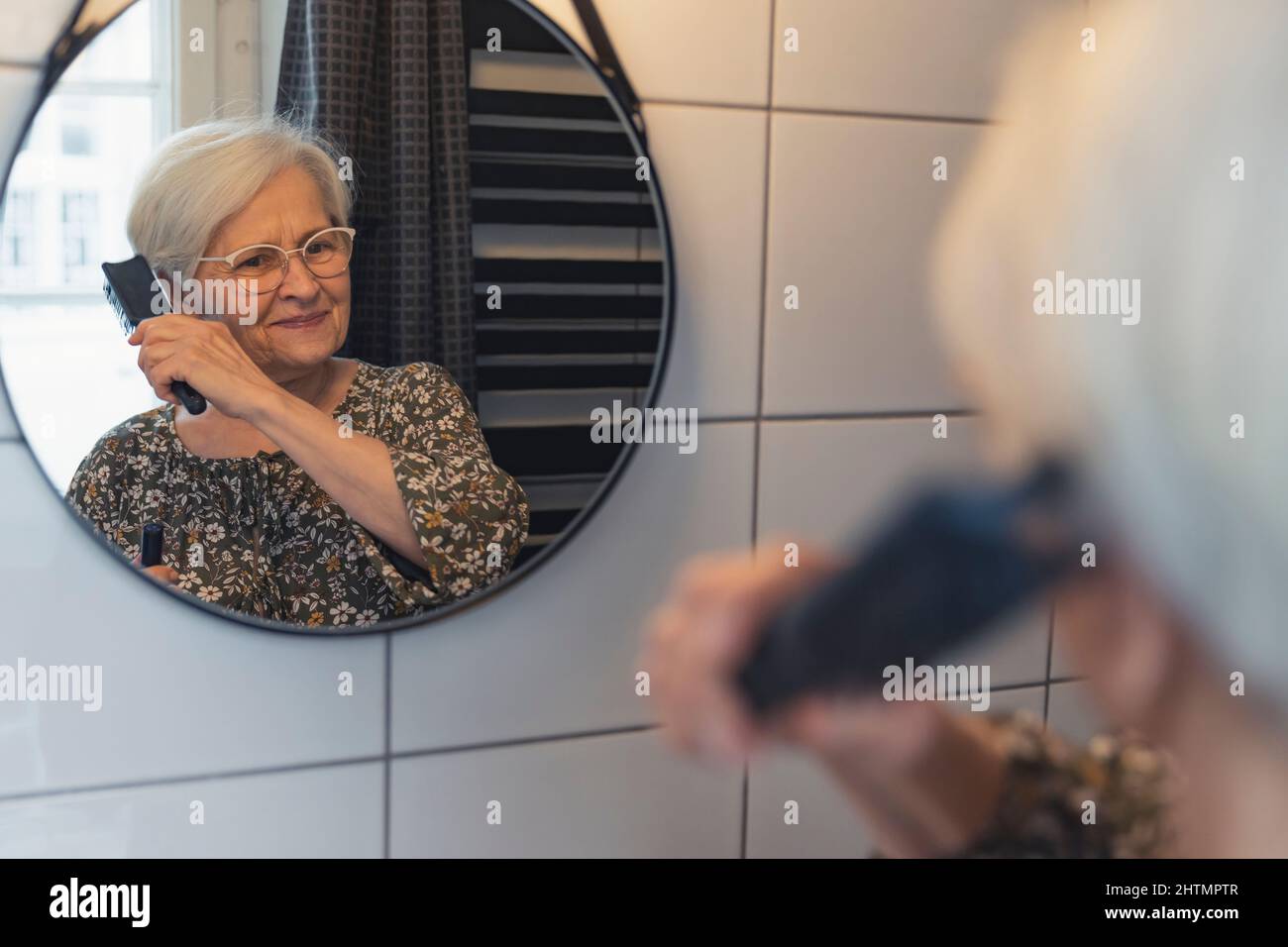 elderly caucasian woman combs her hair and looks at the mirror. High quality photo Stock Photo