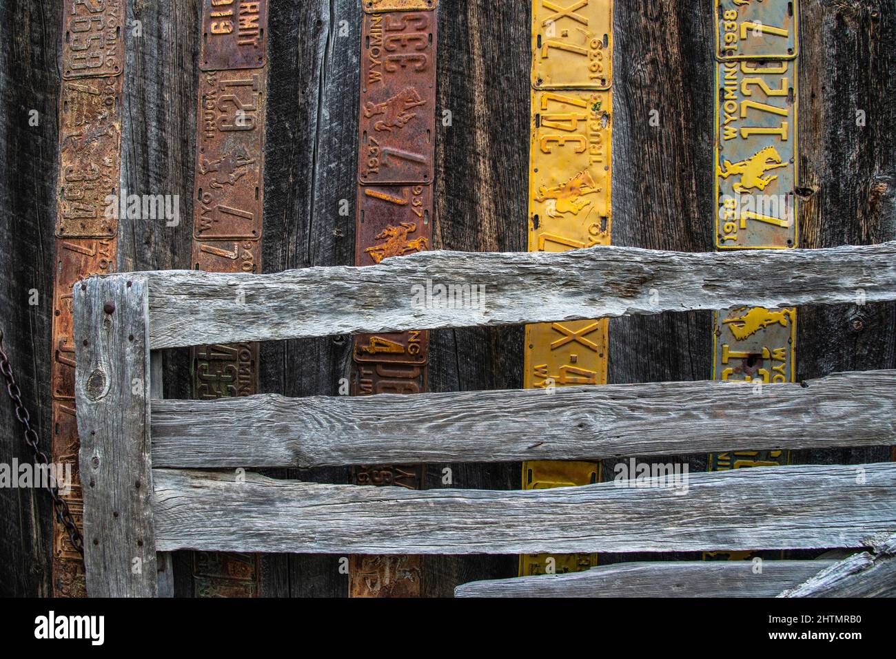old weathered wooden barn with antique Wyoming license plates nailed to the wall for protection and decoration with the old coral gate by the wall Stock Photo