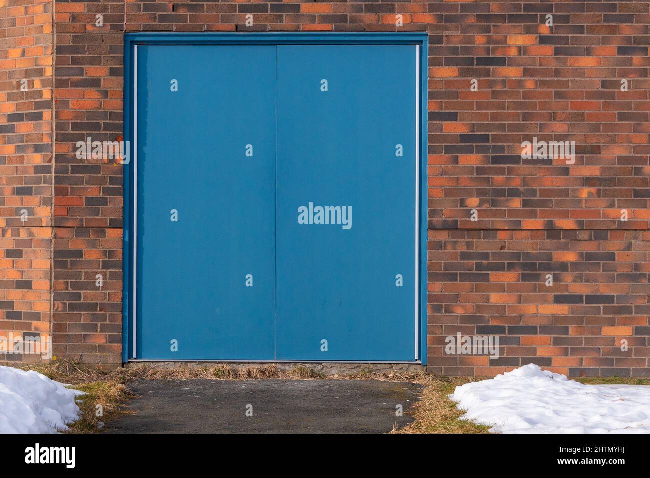Two solid blue metal exterior doors in the entrance of a red and brown building. The doors have no handles and are only opened from the inside. Stock Photo