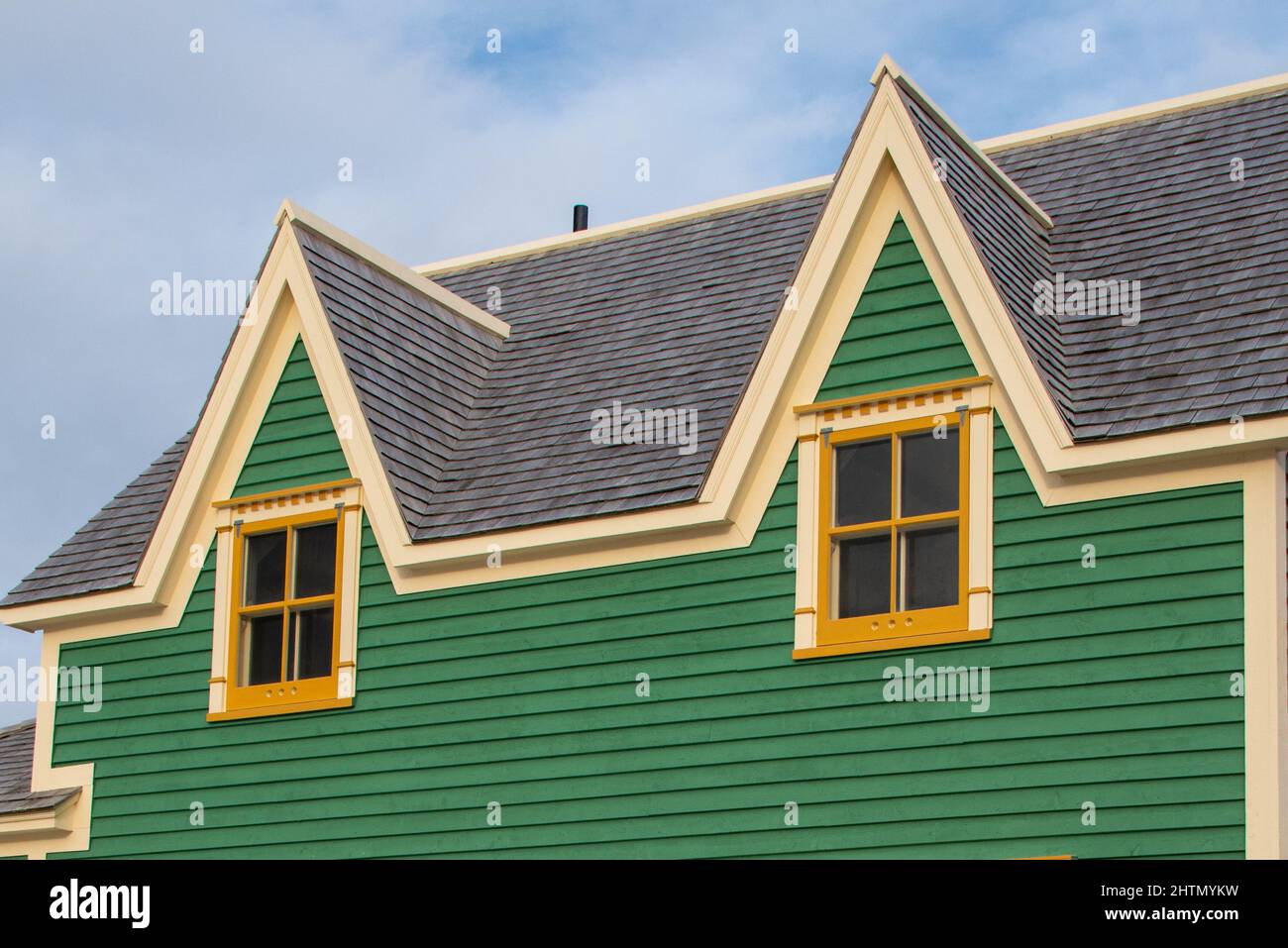 Teal green vintage building with cream trim and dark roof shingles. The top of the building has two dormers and multiple old single hung windows. Stock Photo