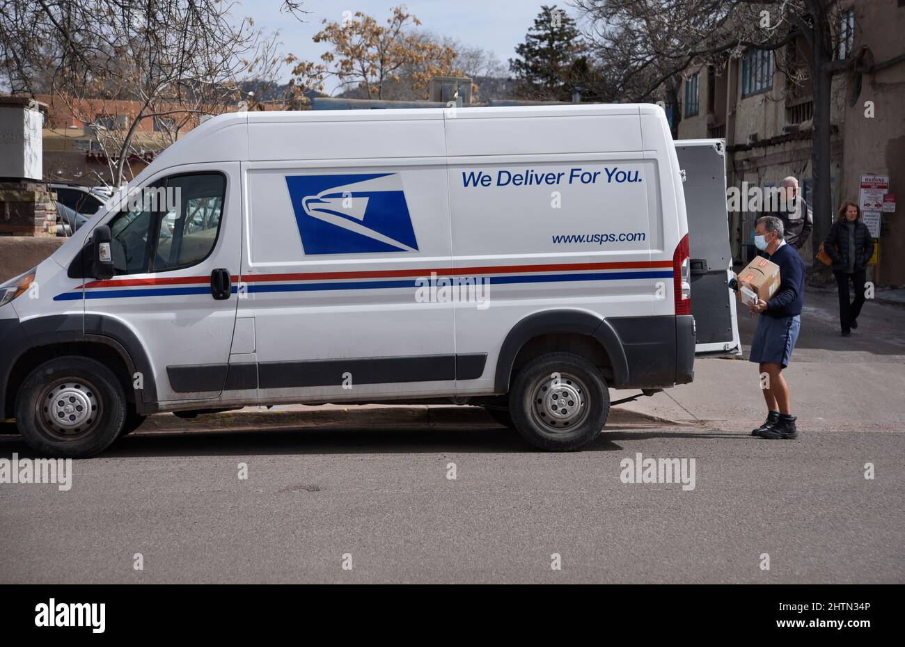 A US postman or mailman delivers a package to a business in Santa Fe, New Mexico. Stock Photo