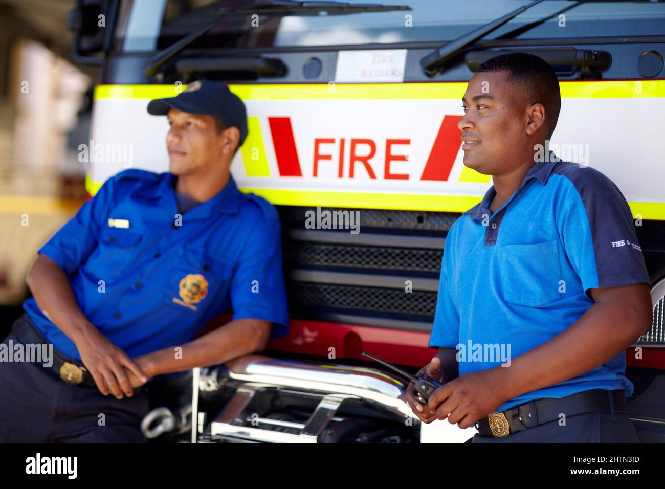 Standing by their faithful firetruck. Shot of two firemen leaning on their truck. Stock Photo