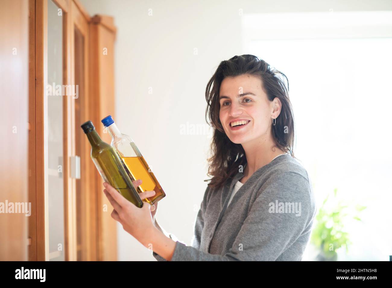 Smiling woman holding two bottles of live oil at home Stock Photo