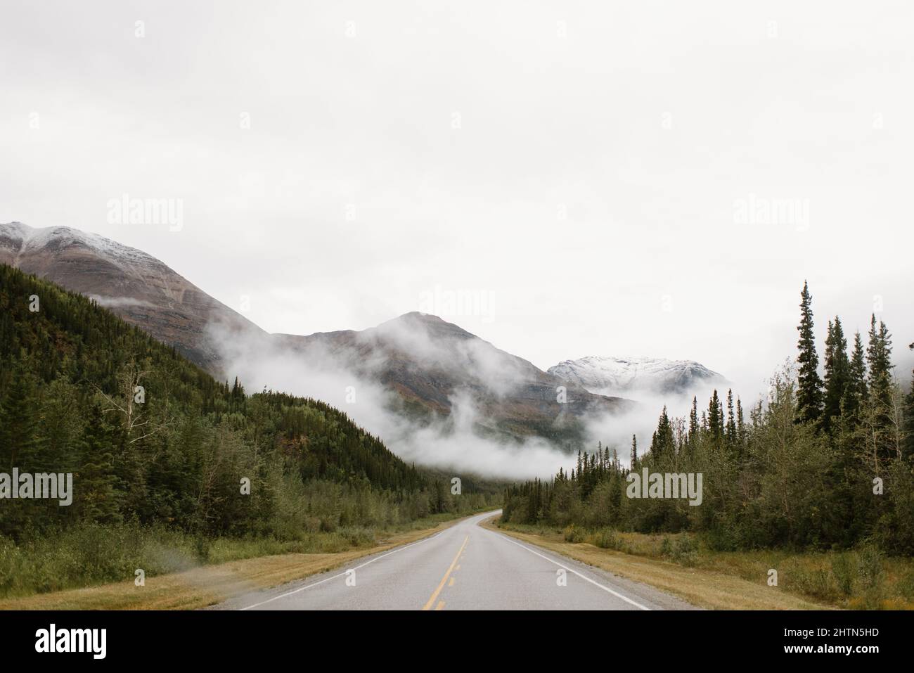 Canada, Yukon, Whitehorse, Empty road crossing hilly landscape in fog Stock Photo