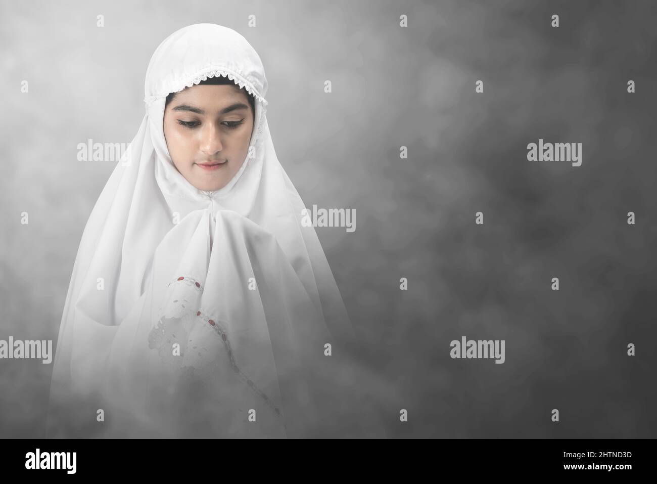 Asian Muslim woman in a veil standing while raised hands and praying ...
