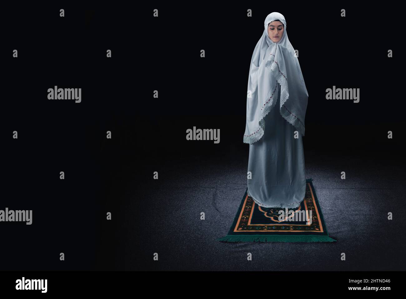 Asian Muslim woman in a veil standing while raised hands and praying ...