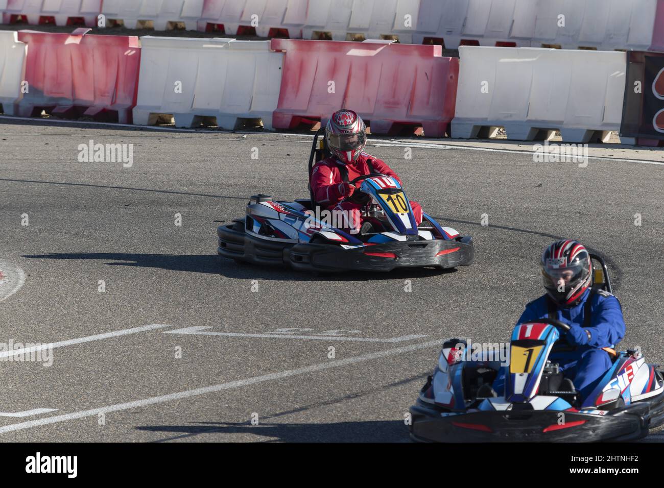 View of two men in helmet driving go-kart on karting circuit at daytime ...
