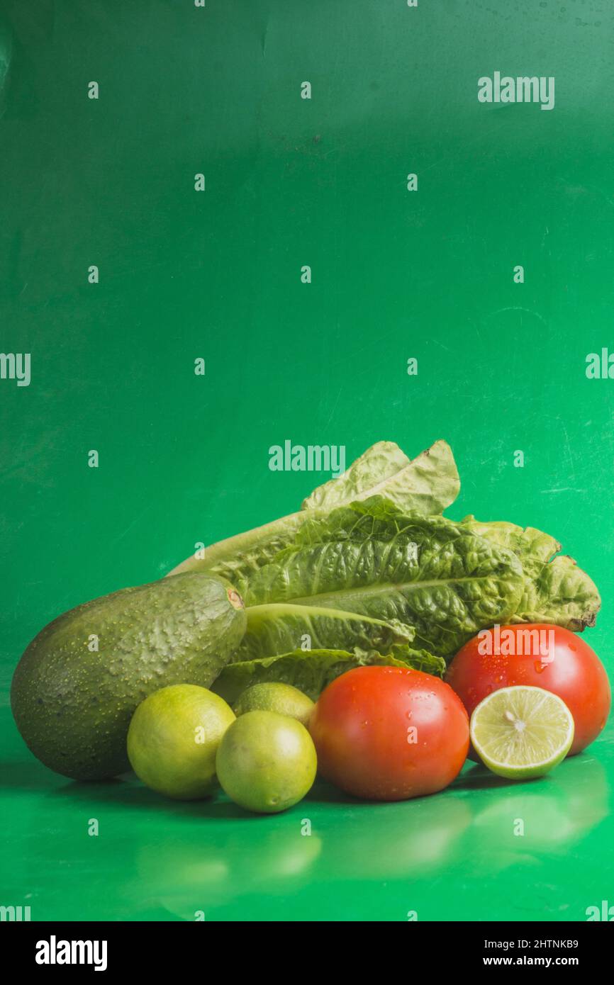 Vertical closeup shot of the limes, tomatoes, avocado and letus on the green background Stock Photo