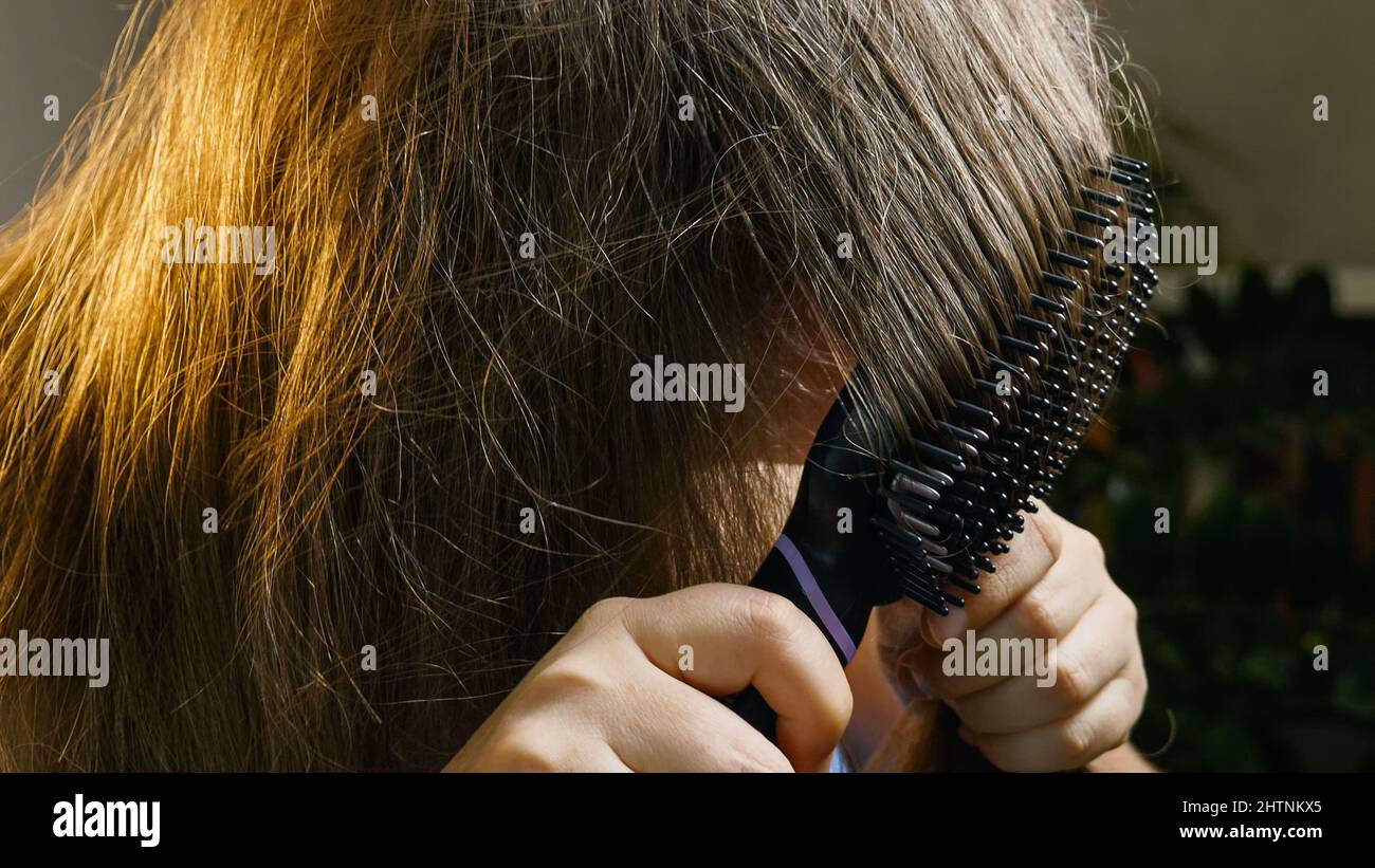 A girl standing in a room brushes her hair with a special electric