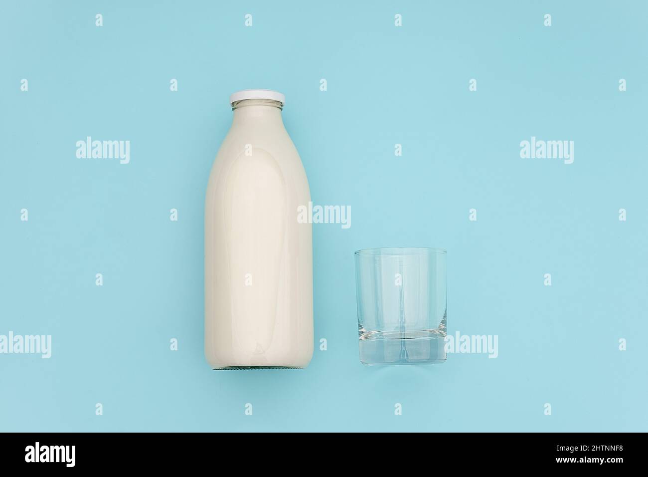 Milk in glass bottle and empty glass on blue background with copy space