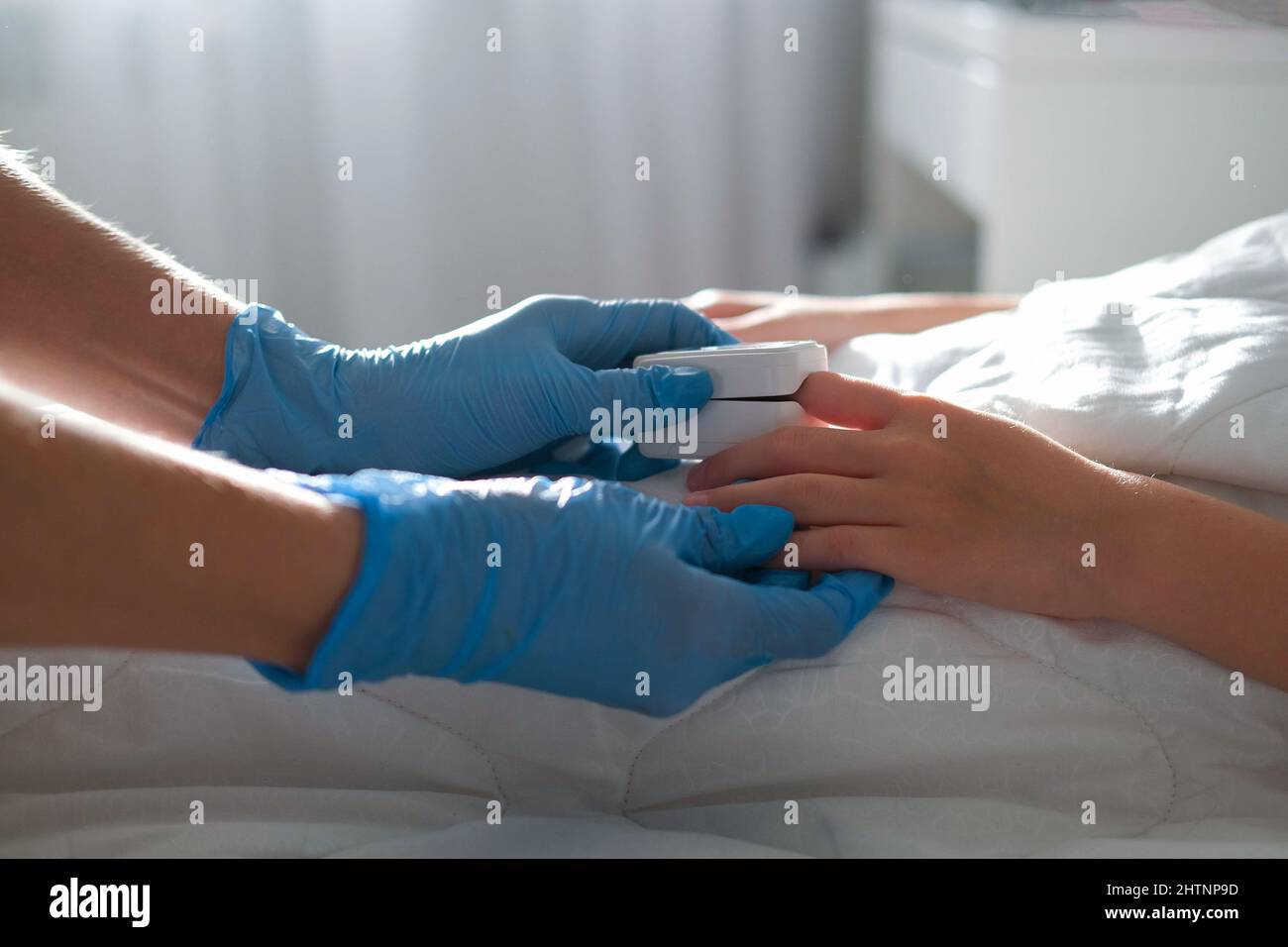 The child lies in bed, a doctor in medical gloves comes up to him and puts a pulse oximeter on