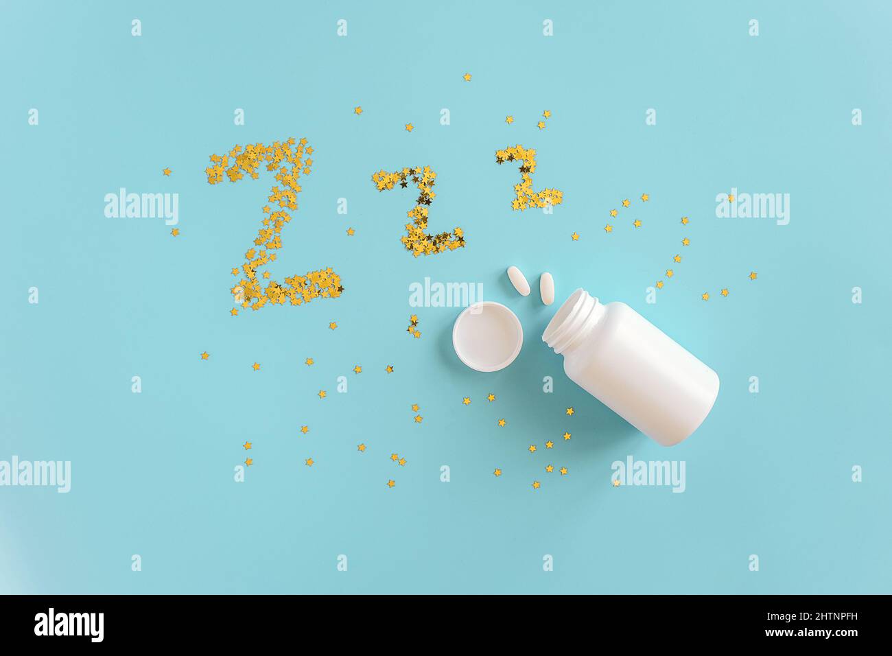 Gold stars confetti fly out white bottle in form of dream symbols Z Z Z on blue background. Concept Insomnia, sleep problems and sleeping pill. Top vi Stock Photo