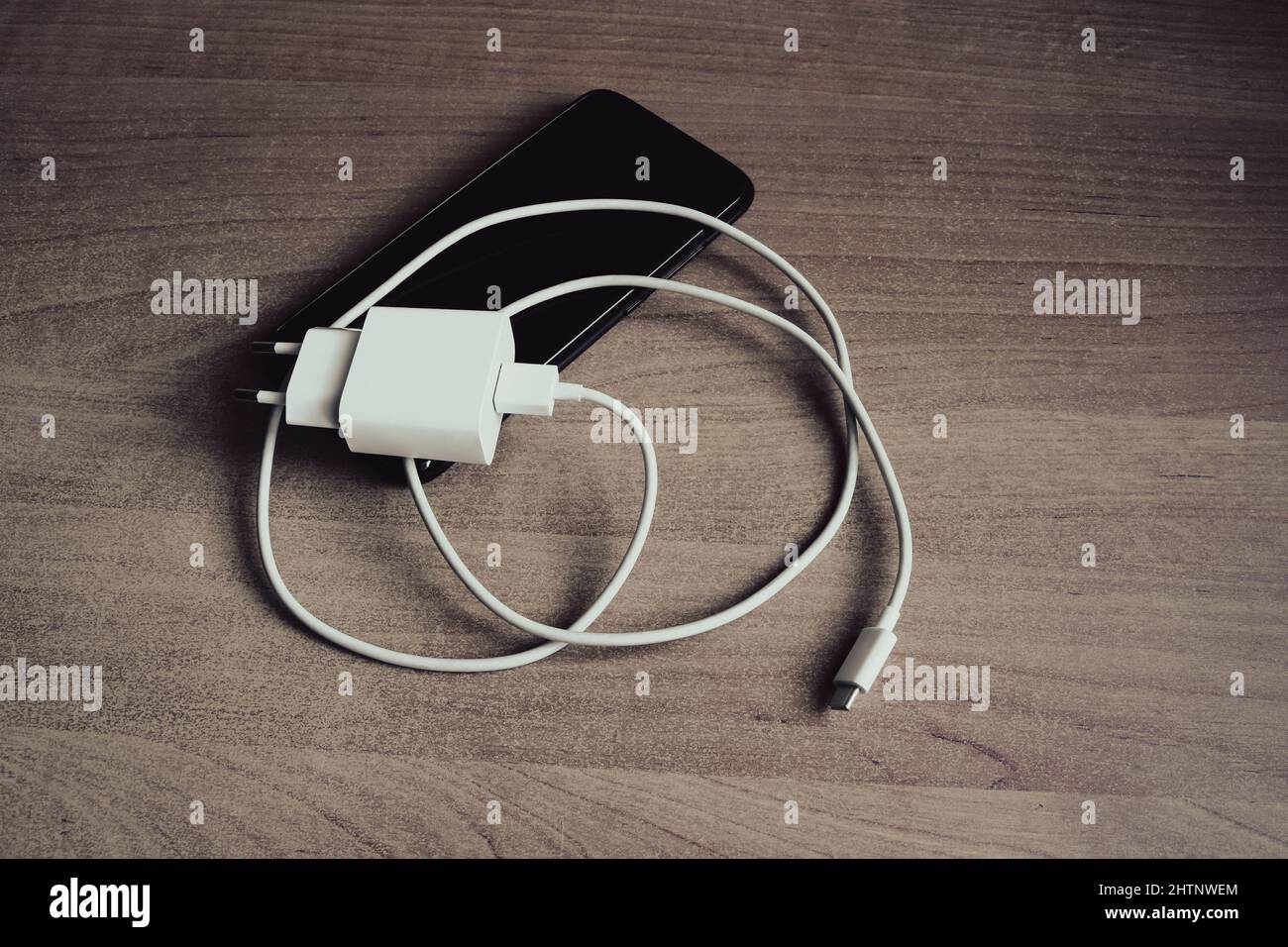 Charger with USB type C cable and smartphone on grunge style wooden table Stock Photo