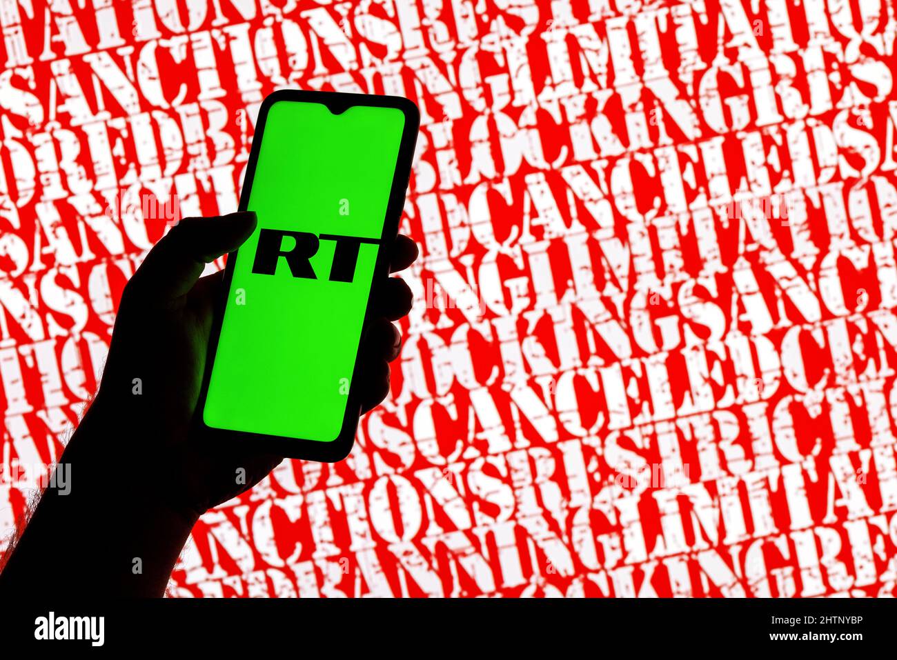 Smartphone with Russia Today logo in hand on background of inscriptions sanctions, censored, banning, blocking and other Stock Photo