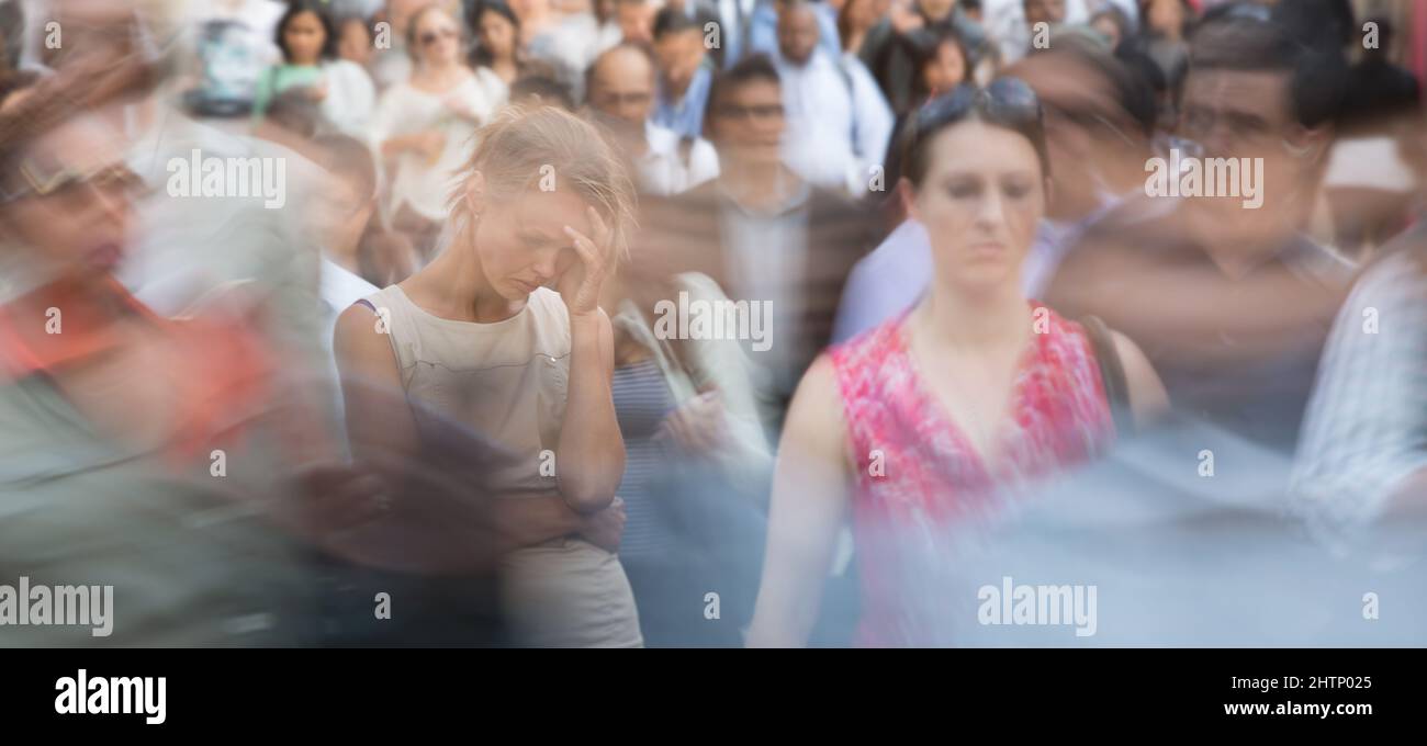 Crowd of people walking on city street - motion blurred image with unrecognizable faces - Young woman standing still, feeling down, depressed Stock Photo