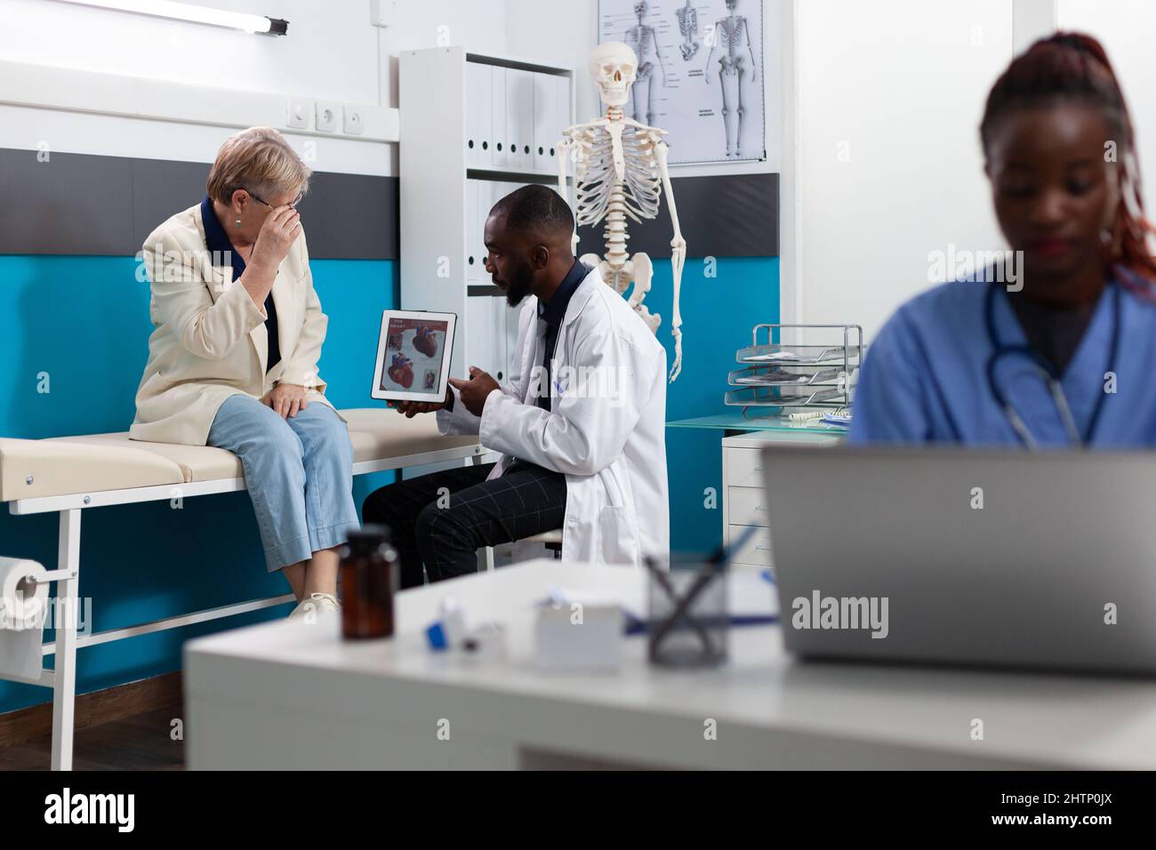 African american therapist doctor showing heart radiography explaining sickness diagnosis to senior woman patient discussing medication treatment in hospital office. Medicine concept Stock Photo