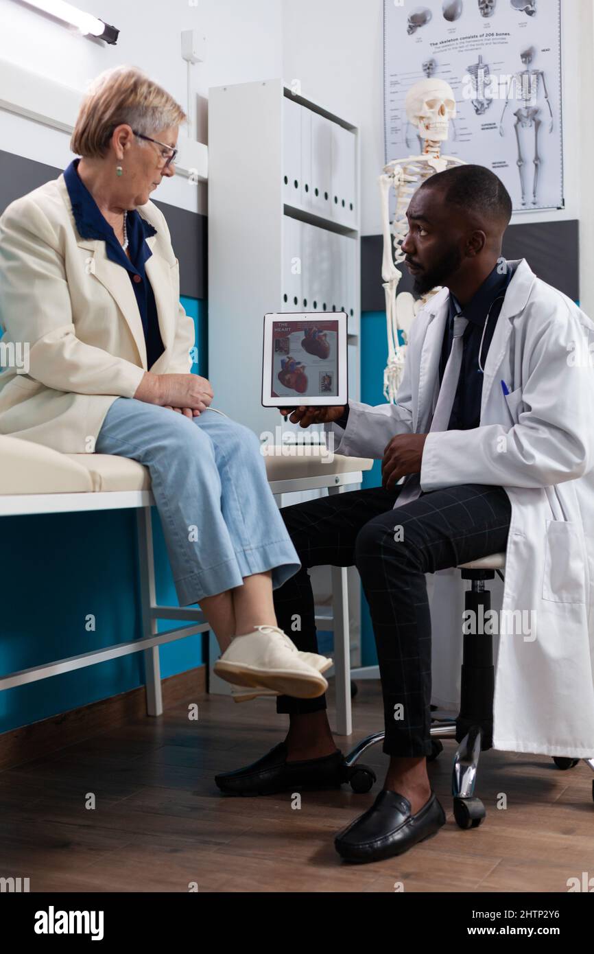 Specialist therapist doctor holding tablet computer explaining heart radiography to senior woman patient discussing healthcare treatment. Medical appointment in hospital office. Medicine concept Stock Photo