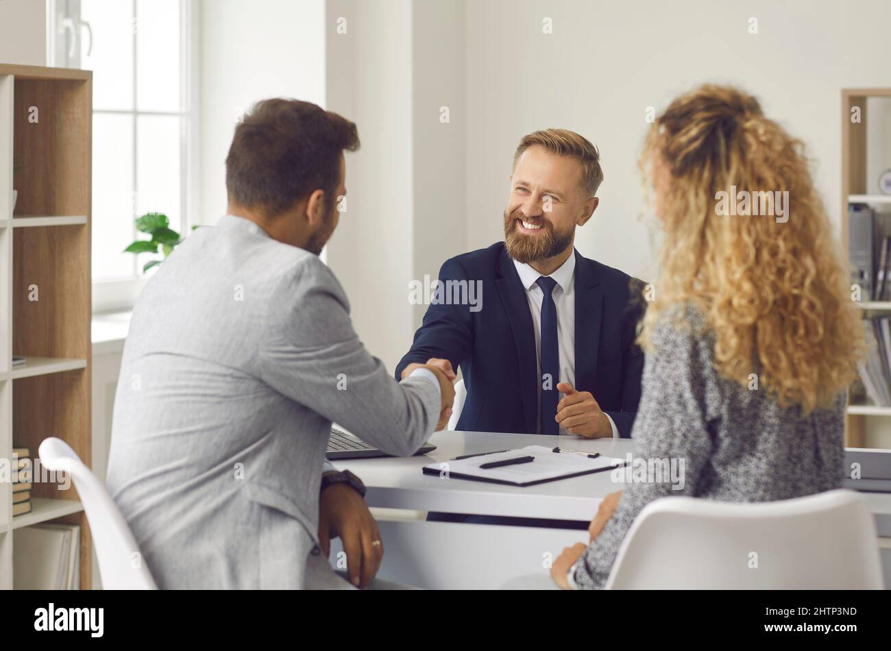Friendly lawyer, realtor or financial advisor shakes hands with his clients to young couple. Stock Photo