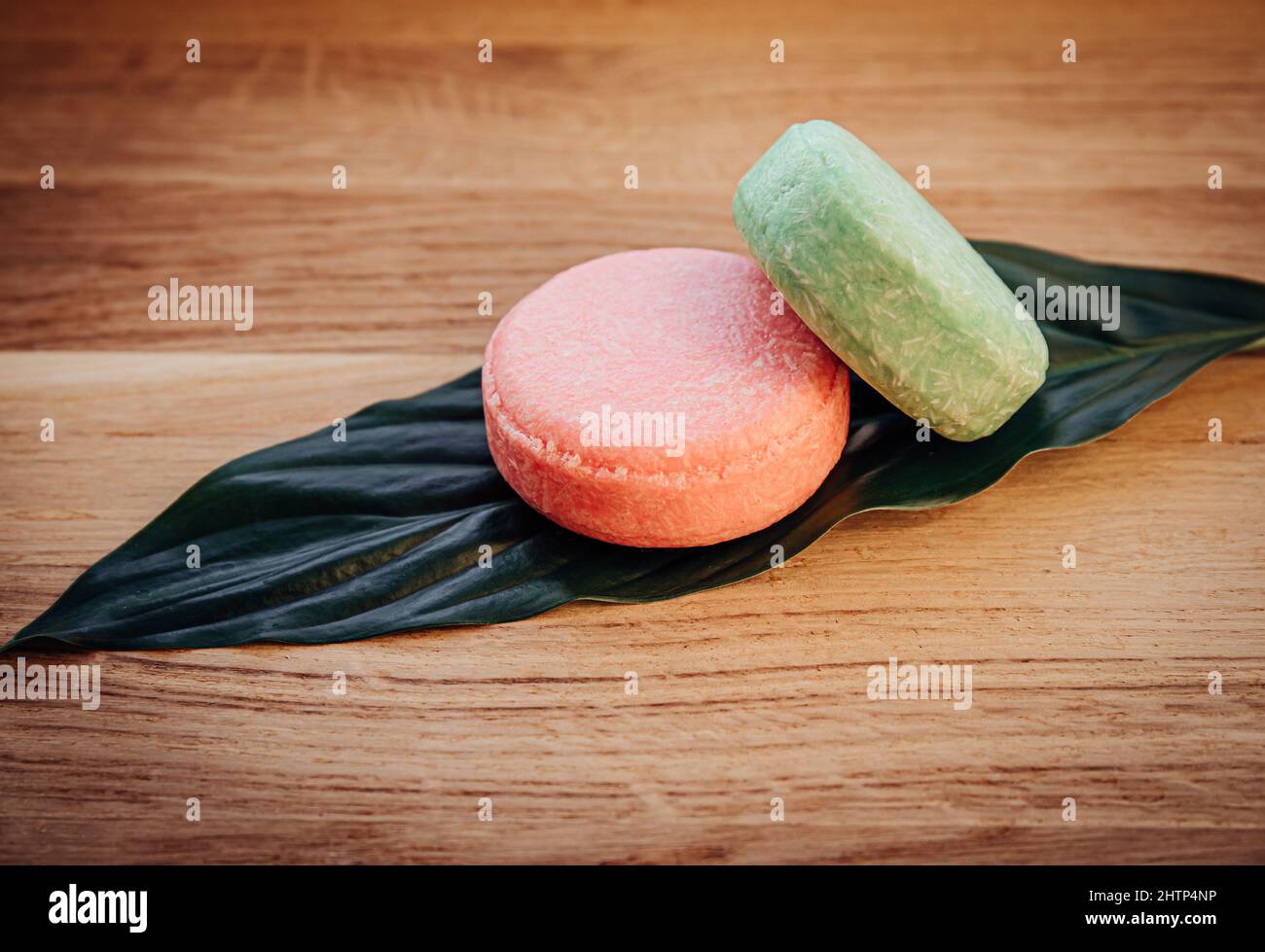 Pink and green color solid shampoo bars or conditioner bar on green leaf on wooden background. Minimalist beauty set indoors, copy space. Stock Photo