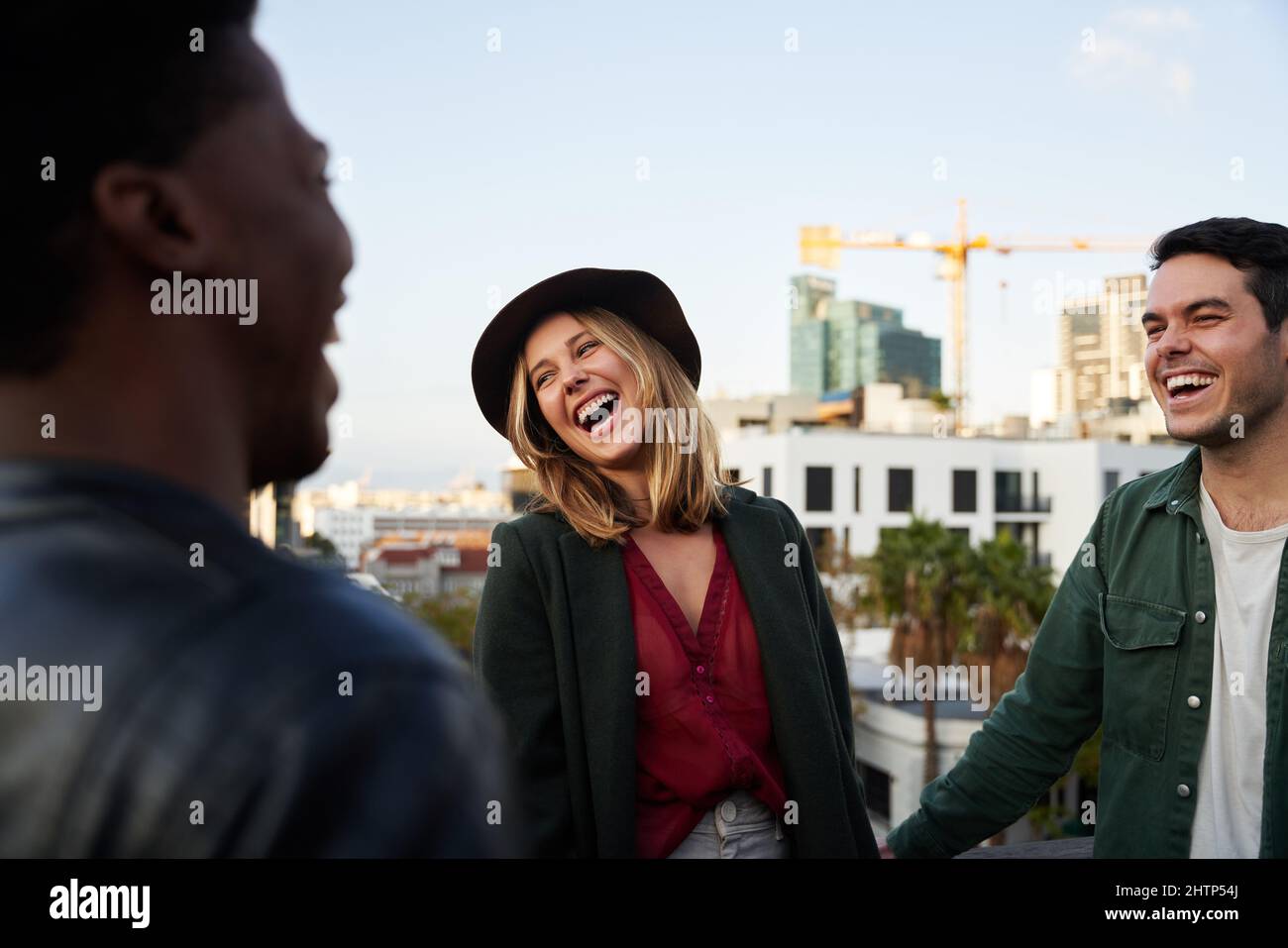 Caucasian female laughing with diverse group of friends socializing on a rooftop terrace at dusk. Stock Photo