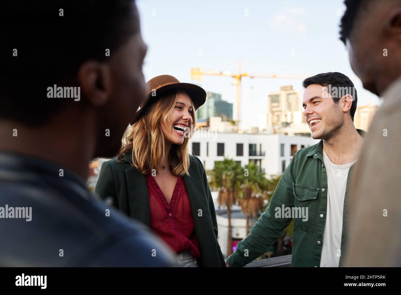 Caucasian female laughing with group of multi-cultural friends socializing on a rooftop terrace at dusk. Stock Photo