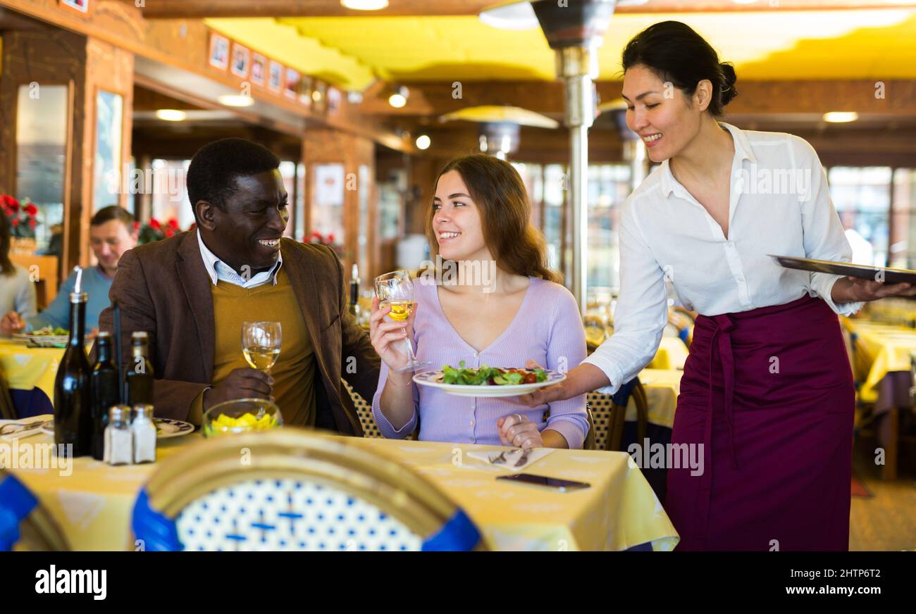 Asian waitress serving ordered dishes to couple in restaurant Stock Photo