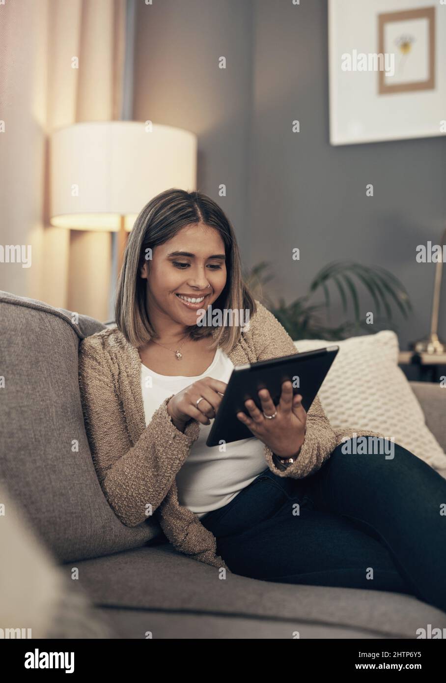 Turning her tablet into a mini tv. Shot of a young woman using a digital tablet on the sofa at home. Stock Photo
