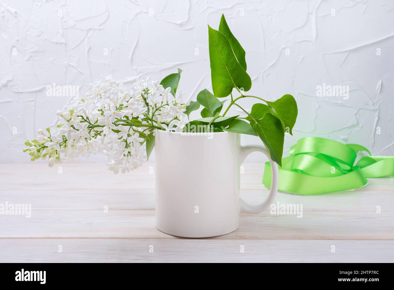 White coffee mug mockup with white lilac and green ribbon. Empty mug mock up for design promotion, styled template Stock Photo