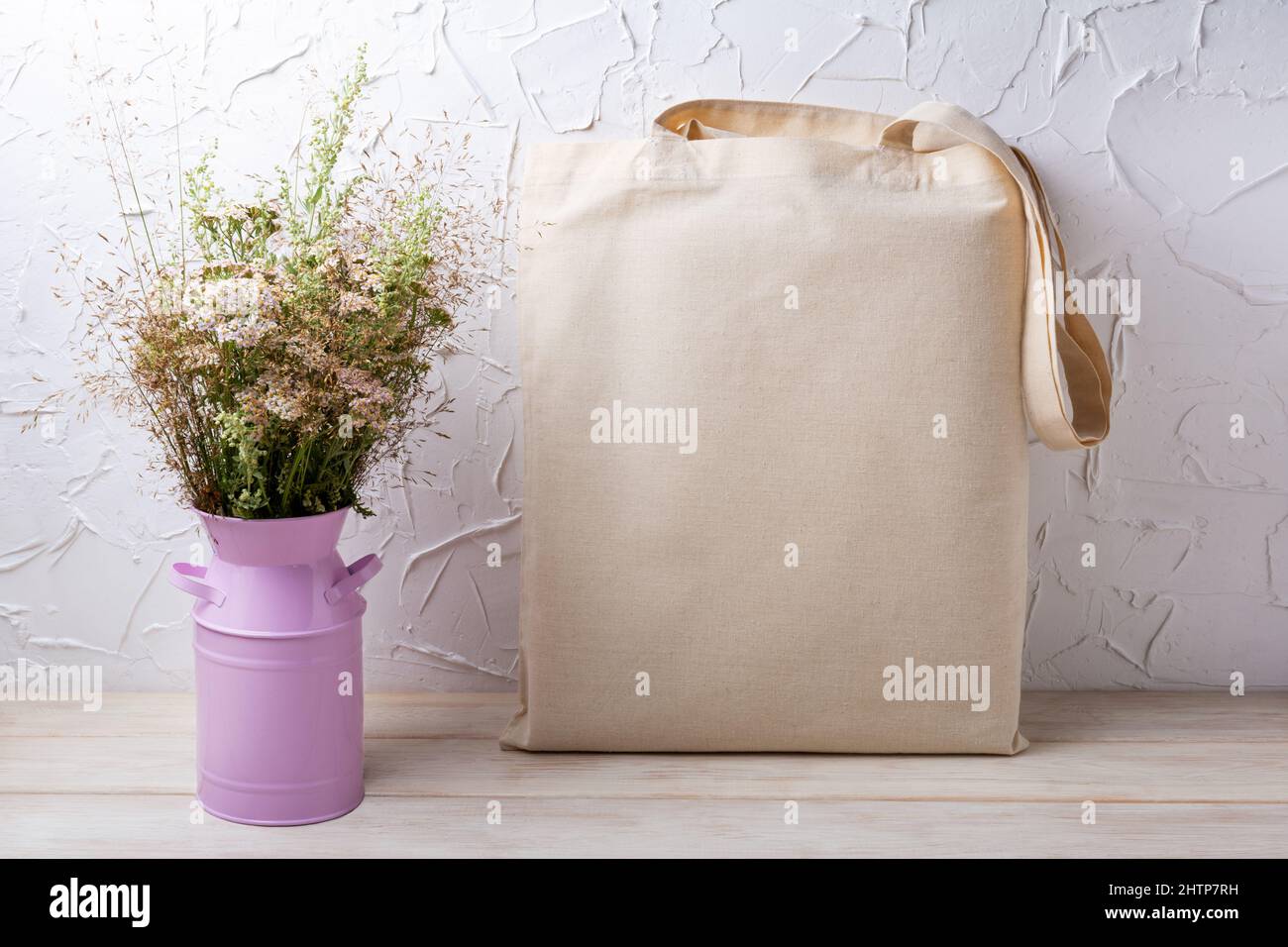 Canvas tote bag mockup with wild flowers and grass in the pink can. Rustic linen shopper bag mock up for branding presentation Stock Photo