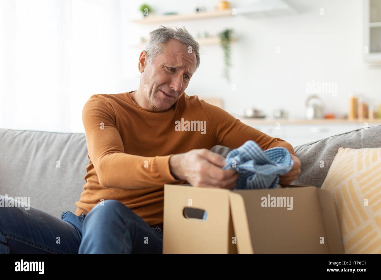 Sad mature man unpacking wrong parcel, delivery mistake concept Stock Photo