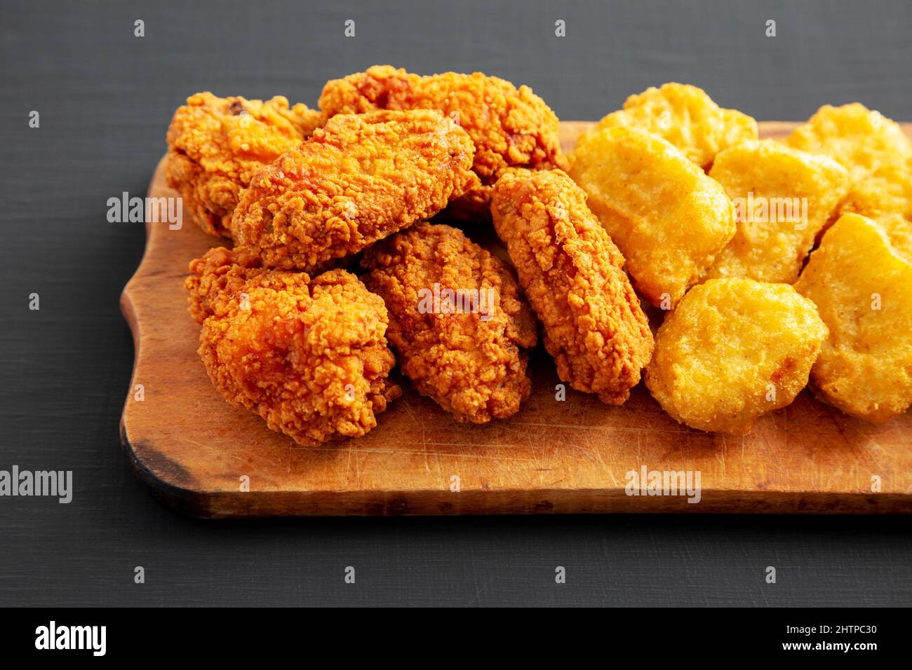 Homemade Crispy Fried Chicken Wings and Nuggets on a rustic wooden board on a black background