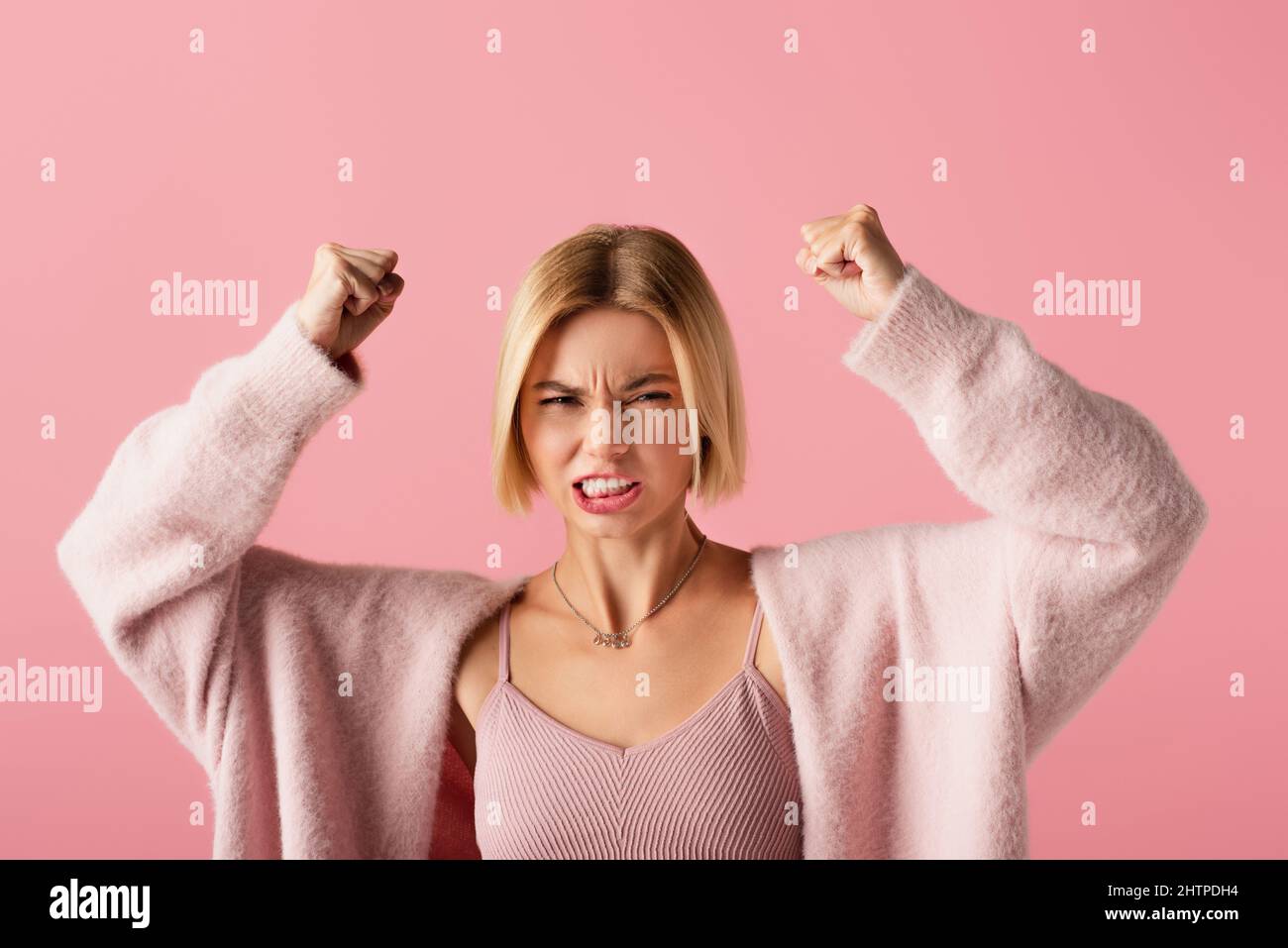 angry young woman in soft cardigan with clenched fists isolated on pink,stock image Stock Photo