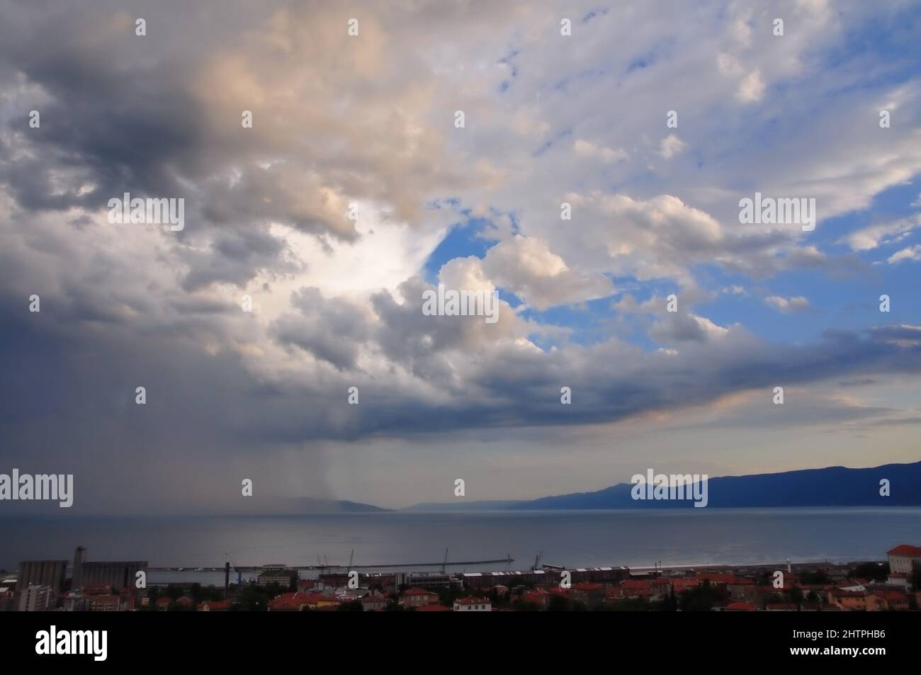 Stormy sky over sea and City. Rijeka bay and rain coming. Rain curtain over sea in Rijeka bay.Dramatic landscape of stormy sky over small seaside city Stock Photo