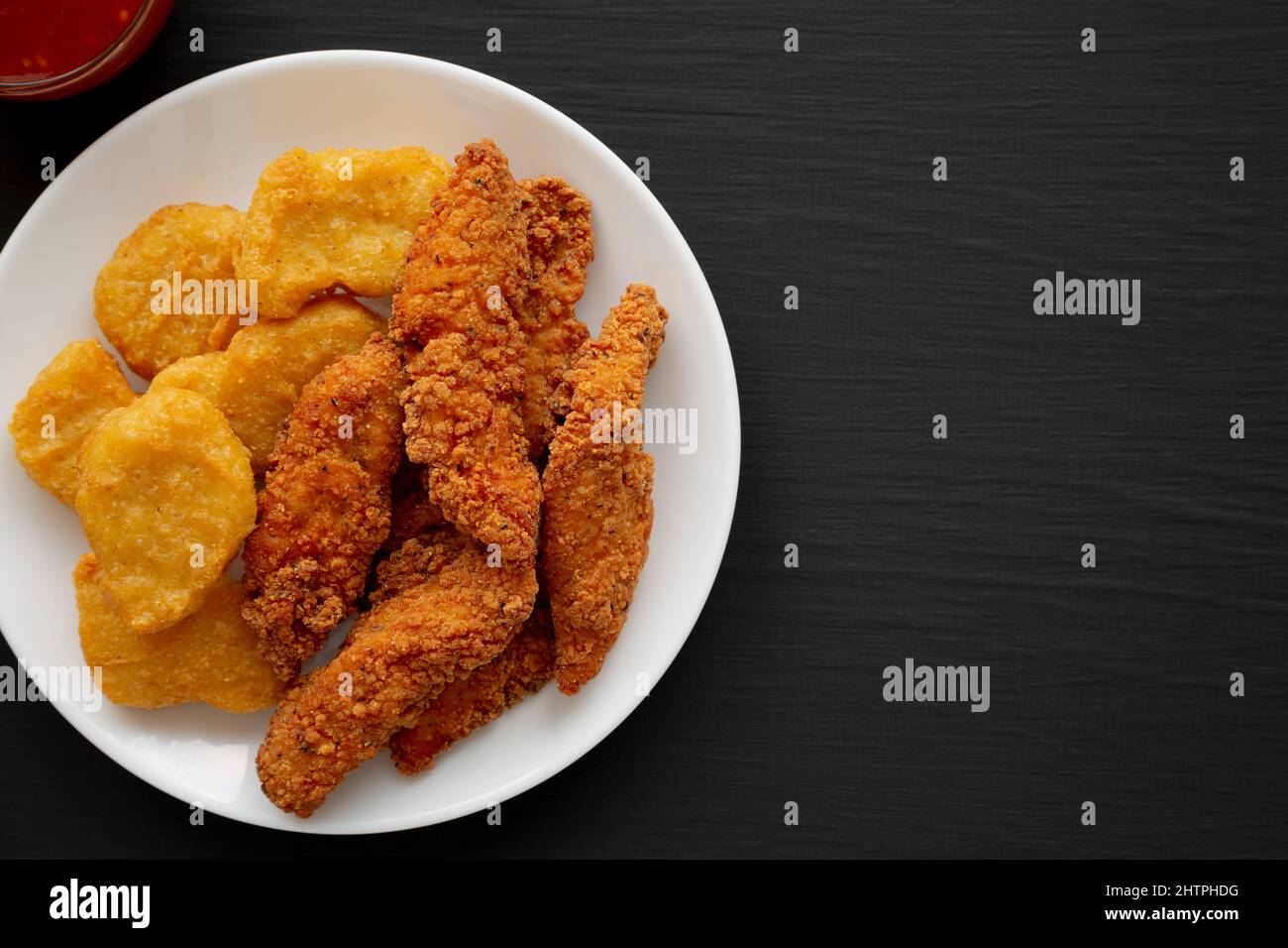 Homemade Nuggets and Chicken Tenders with Sweet and Sour Sauce on a black background, top view