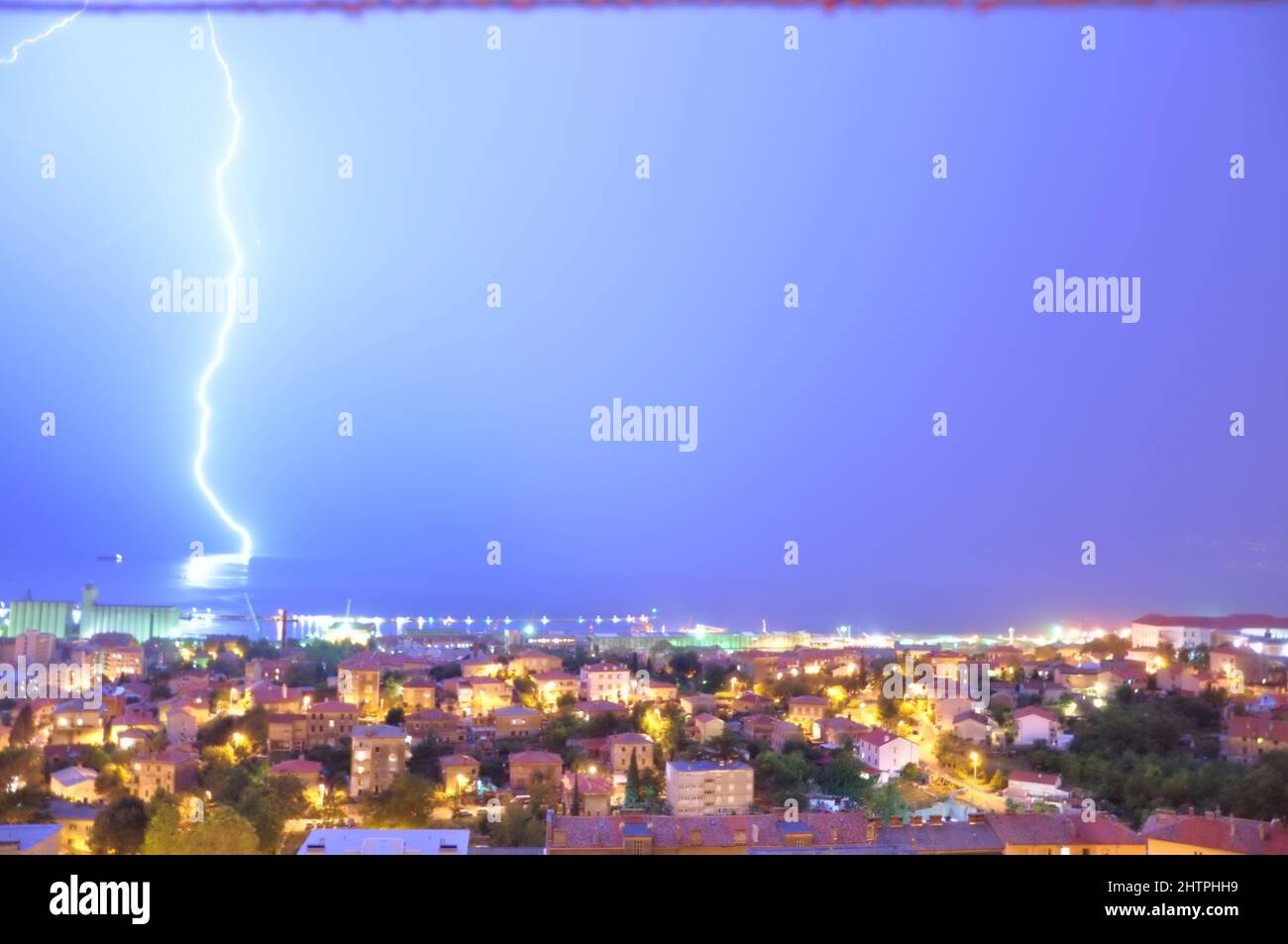 Nig storm with one lightening bolt hitting Adriatic sea in Rijeka bay, Croatia. Spectacular lightning bolts over a calm sea bay. Stock Photo
