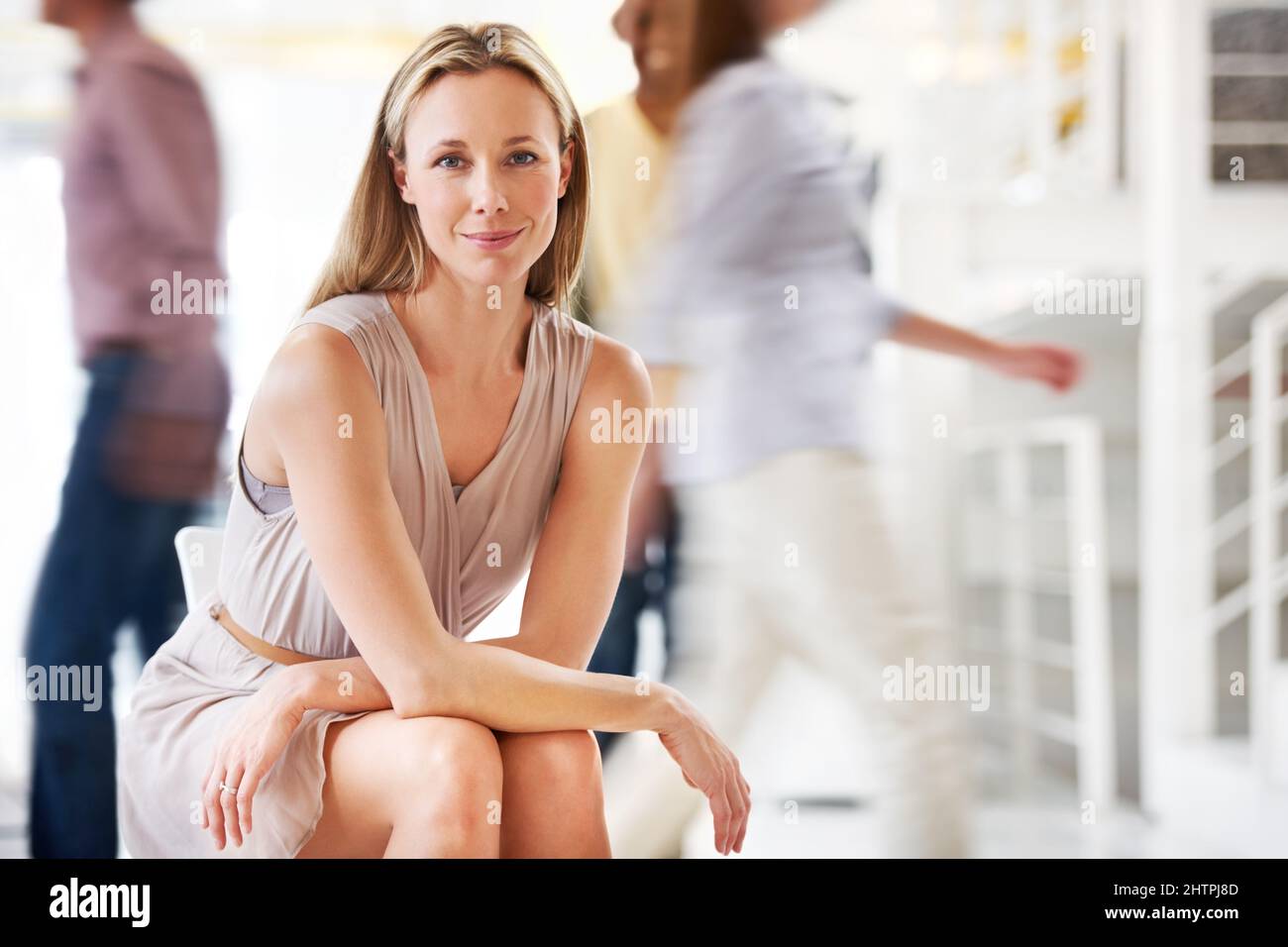Shes got poise amidst the hustle. A pretty mature businesswoman sitting calmly as his colleagues stream by in haste - conceptual. Stock Photo