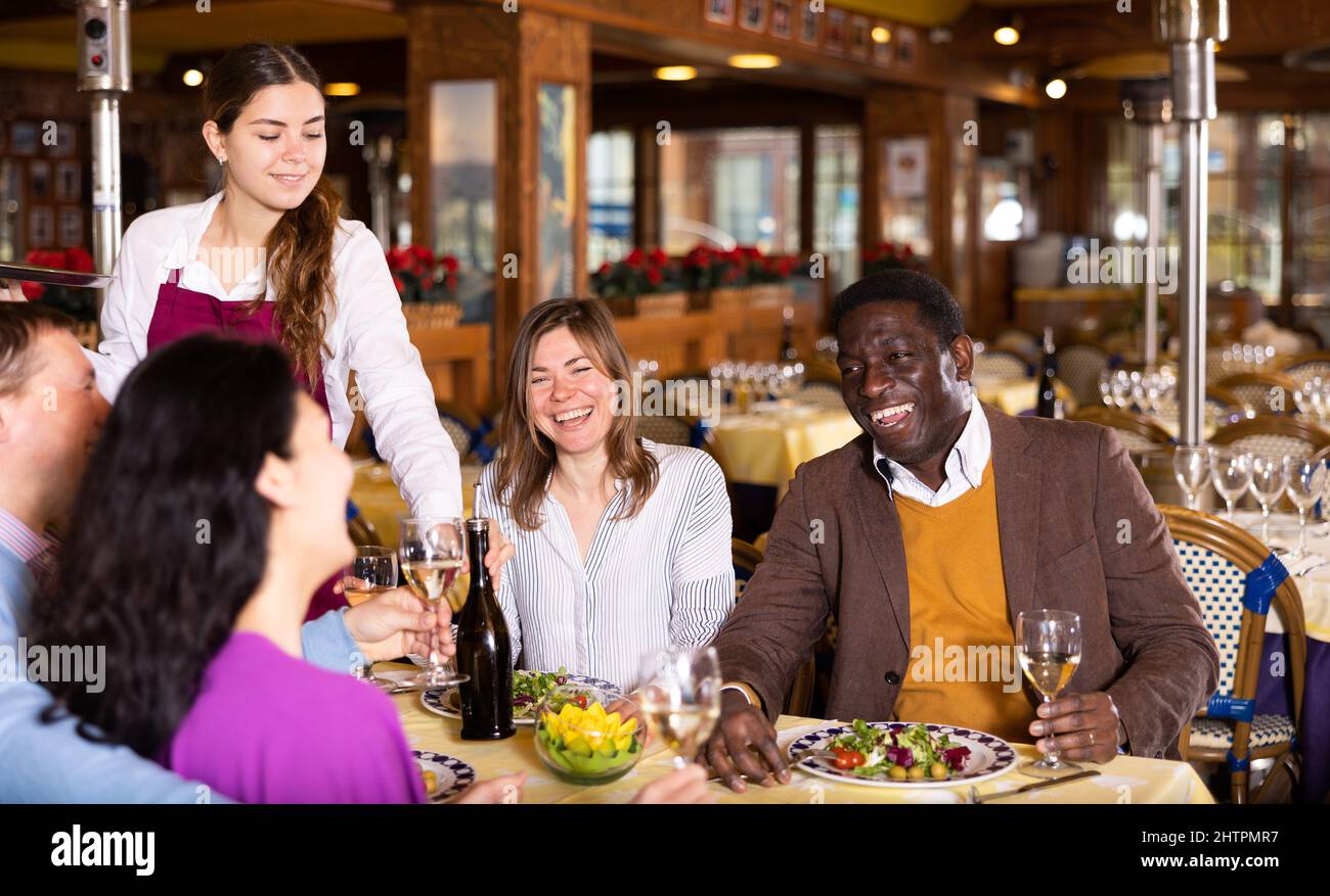 Young waitress serving cheerful people during dinner in restaurant Stock Photo