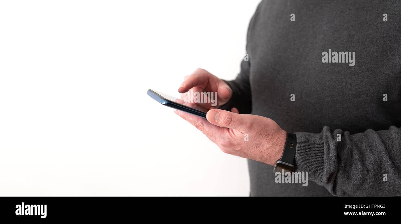 midsection of man holding smartphone in hand in front of white wall Stock Photo