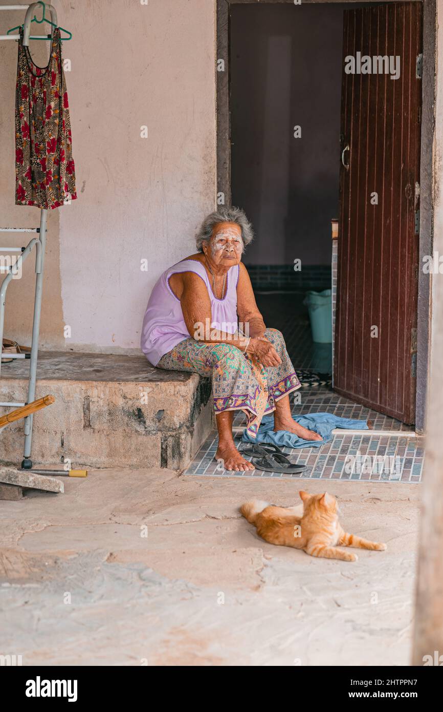 Old woman with thanaka paste on her face sitting near door of her house Thailand Stock Photo