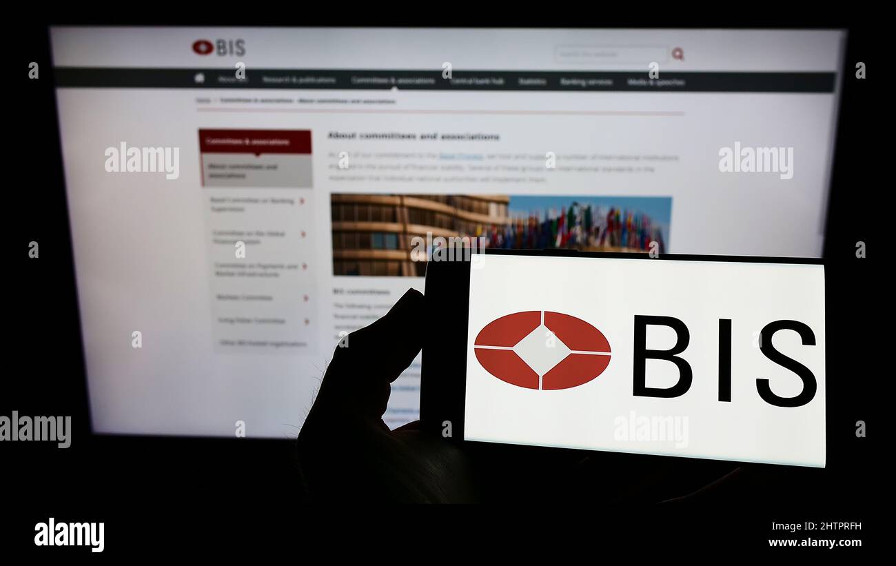 Person holding cellphone with logo of Bank for International Settlements (BIS) on screen in front of business webpage. Focus on phone display. Stock Photo