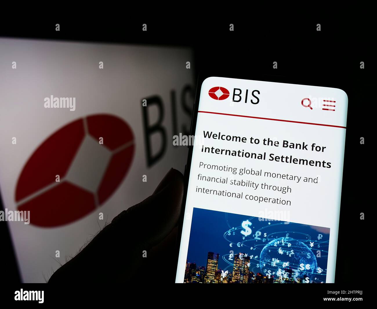 Person holding cellphone with webpage of Bank for International Settlements (BIS) on screen in front of logo. Focus on center of phone display. Stock Photo