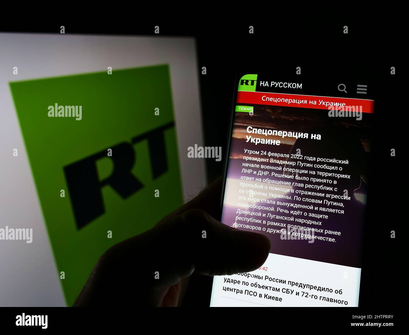 Person holding cellphone with webpage of Russian state-controlled television company RT on screen with logo. Focus on center of phone display. Stock Photo