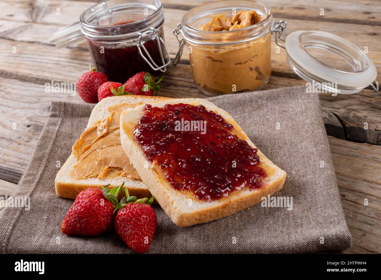 Open face peanut butter and jelly sandwich on napkin with jars and strawberries at table Stock Photo