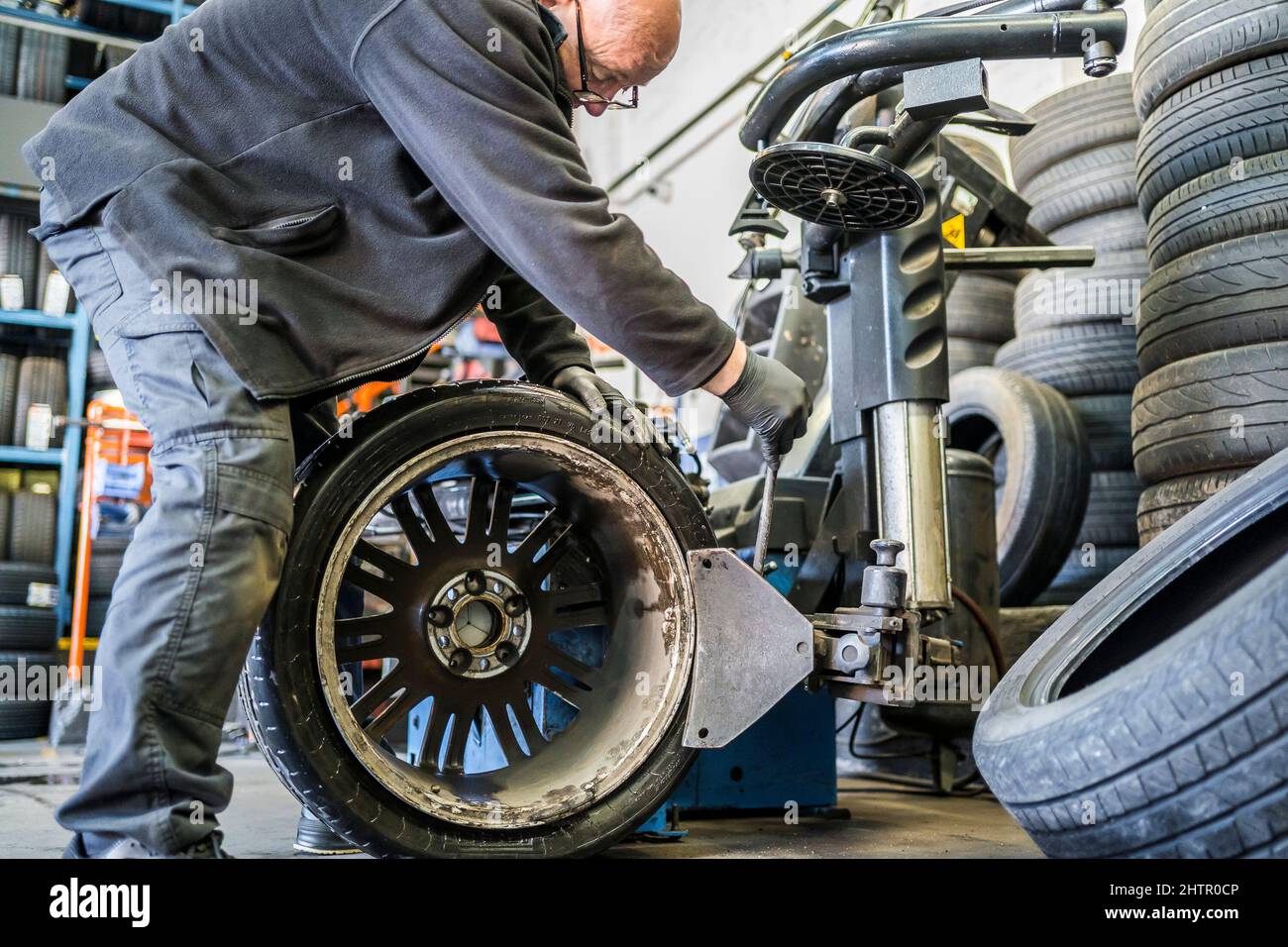 UK tyre garage workshop. Garage mechanic removing a car tyre on an alloy wheel using a vehicle tyre changing machine. Stock Photo