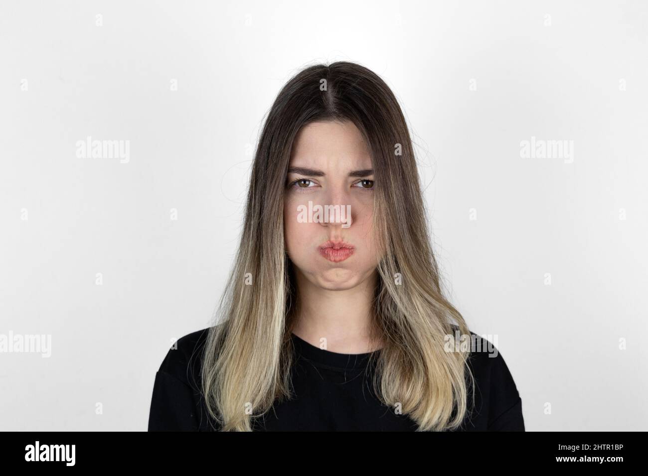 Close up photo of bored girl. She is blowing her cheek against white background. White background. Mouth inflated with air, crazy expression. Stock Photo