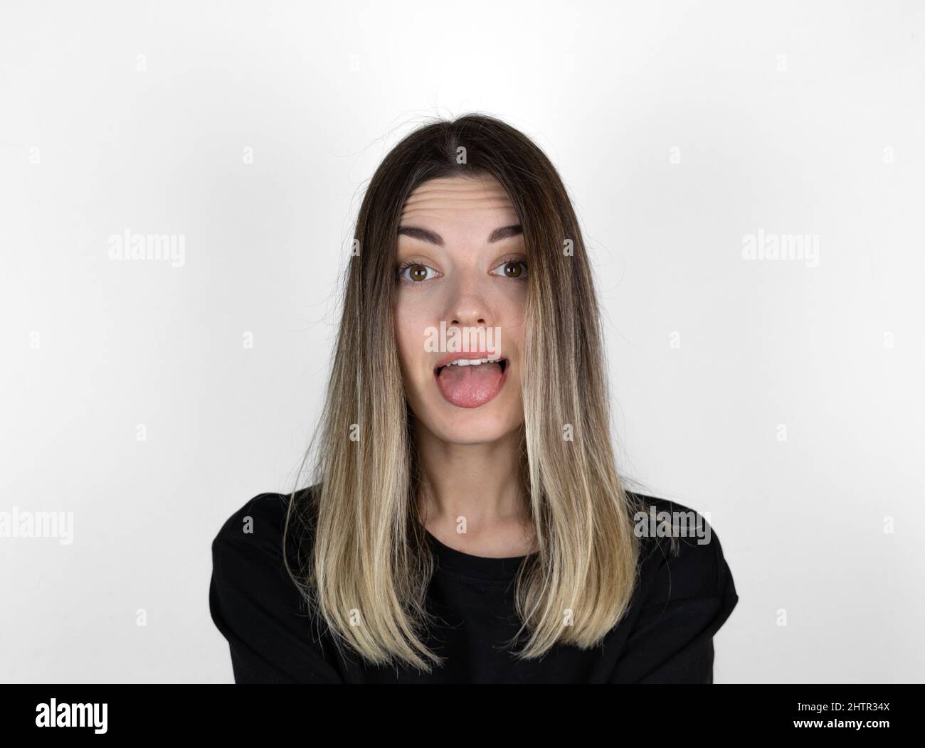 Young woman sticking out tounge, close up portrait. Teasing you through camera while isolated with white background. Stock Photo
