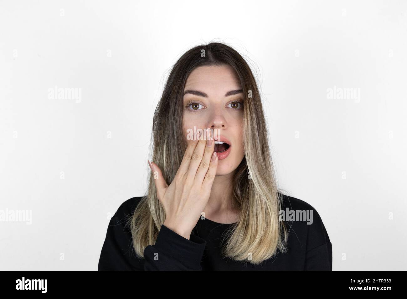 Shocked girl covering mouth with hand. 'Is that for real?!' concept photo on white background. She is looking right.  Text space. Stock Photo