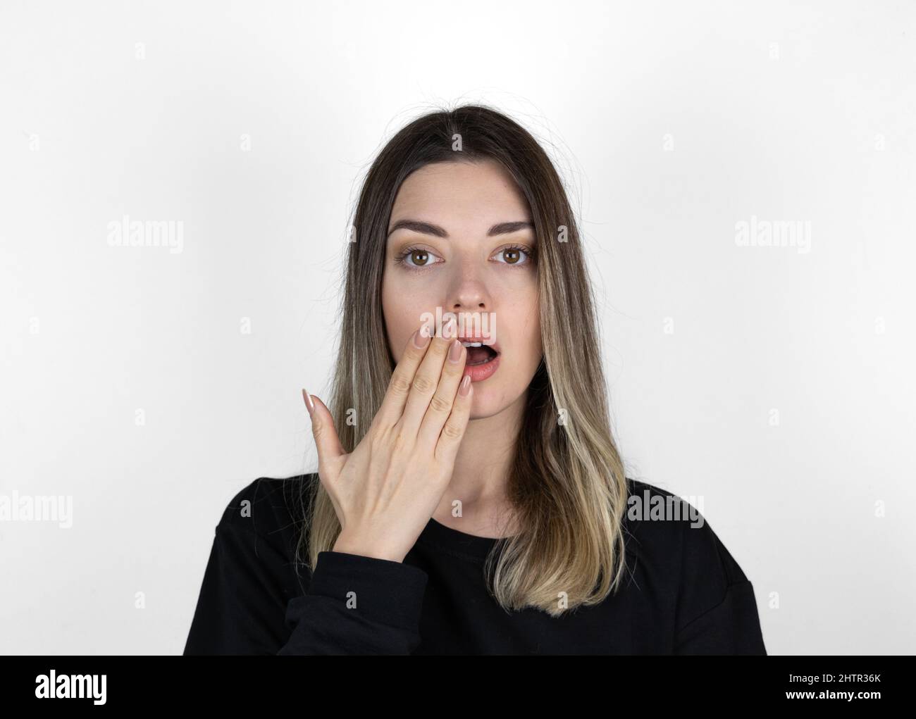Shocked girl covering mouth with hand. 'Is that for real?!' concept photo on white background. She is looking right.  Text space. Stock Photo