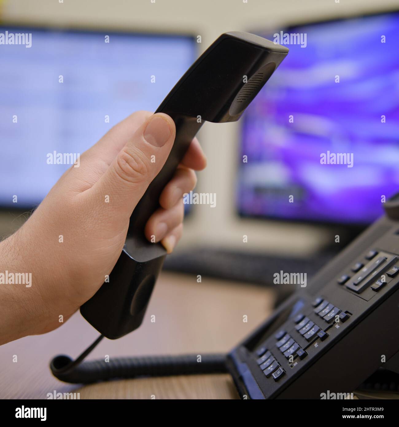 A man hand holds a phone near the monitors of office computers ...